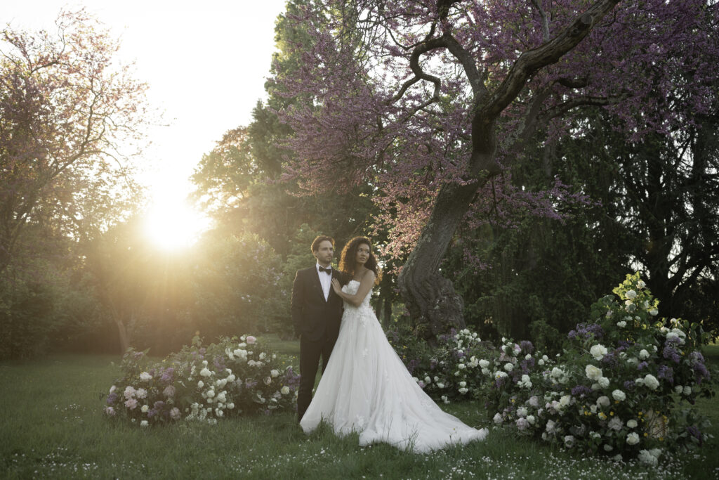 Bride and groom at golden hour under a blooming Judas tree with luxurious lilac and peony floral arrangements in a château wedding in the Loire Valley.