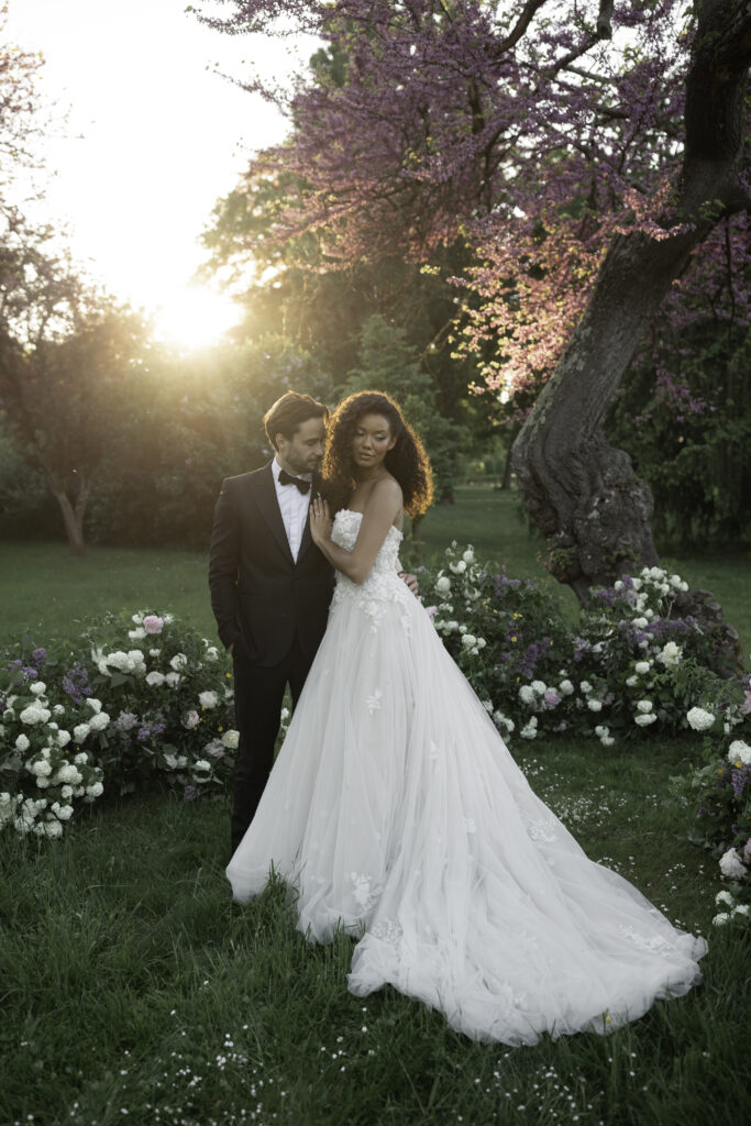 Bride and groom at golden hour under a blooming Judas tree with luxurious lilac and peony floral arrangements in a château wedding in the Loire Valley.