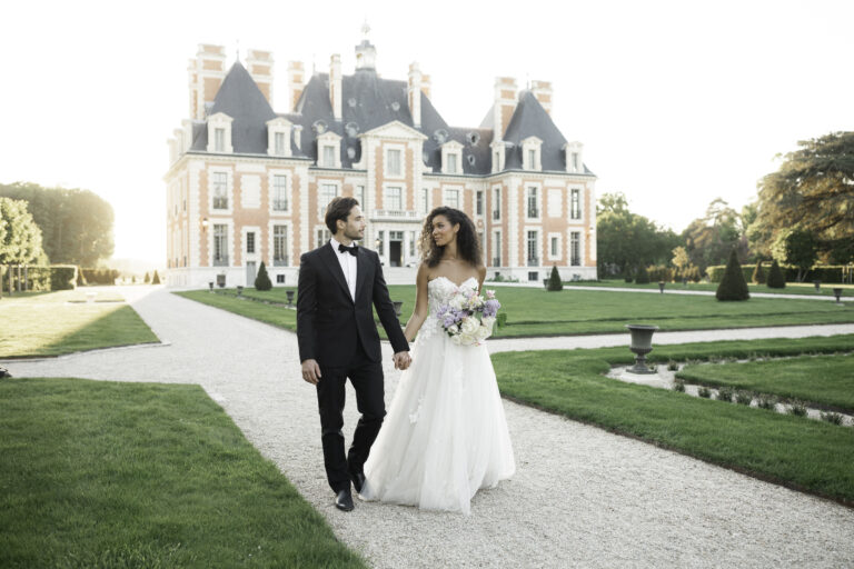 Bride and groom walking hand in hand in front of Château de Nainville during a luxury destination wedding in France